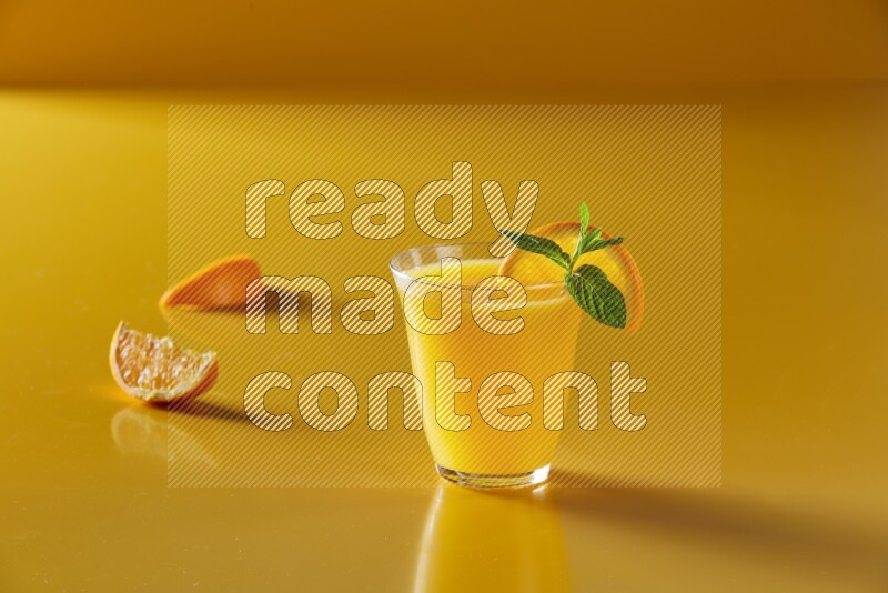 glass of orange juice with orange & mint  on yellow background