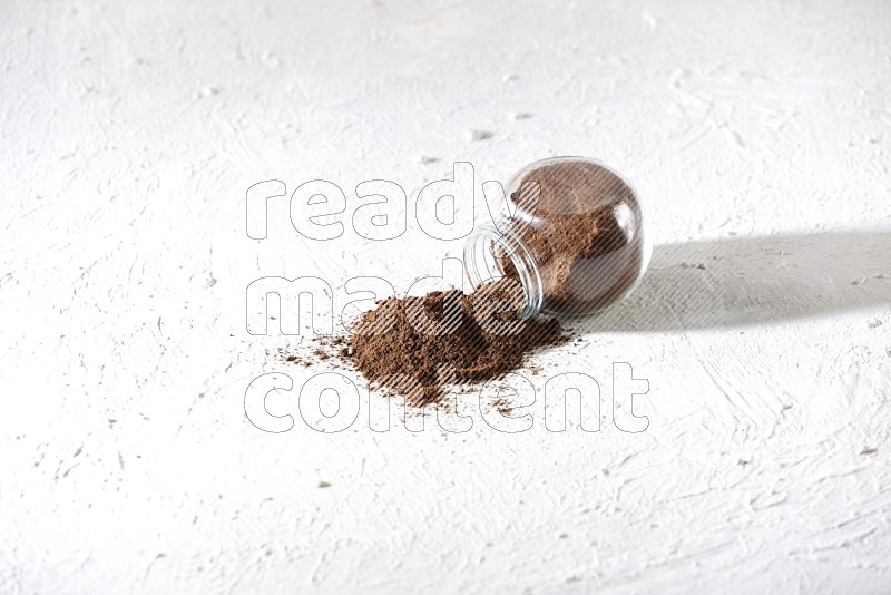 A flipped glass spice jar full of cloves powder and powder came out of it on textured white flooring