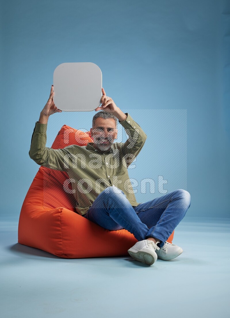 A man sitting on a orange beanbag and holding social media sign