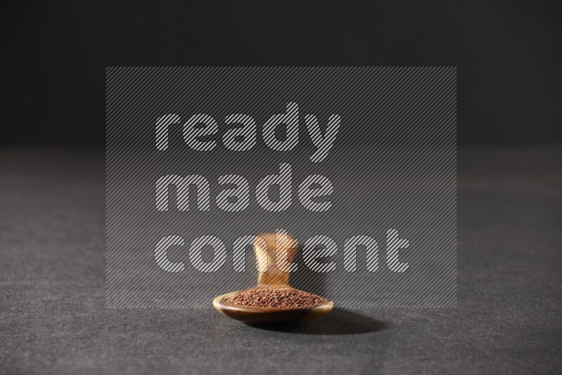 A wooden ladle full of garden cress seeds on a black flooring