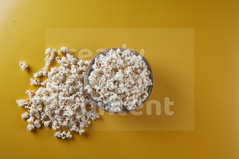 A brown pottery bowl full of popcorn with popcorn beside it on a yellow background in different angles