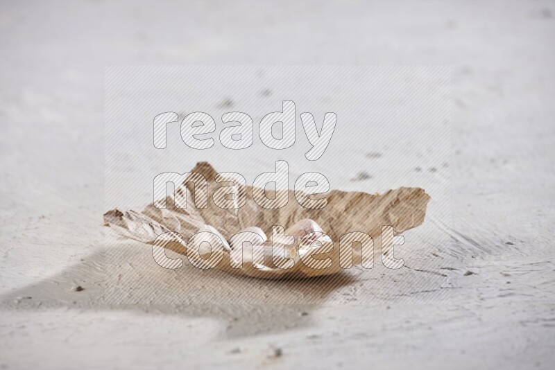 A crumpled piece of paper full of garlic cloves placed on a textured white flooring