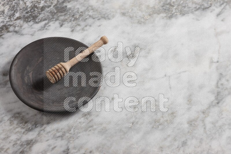 Black pottery plate with wooden honey dipper in it on grey marble background