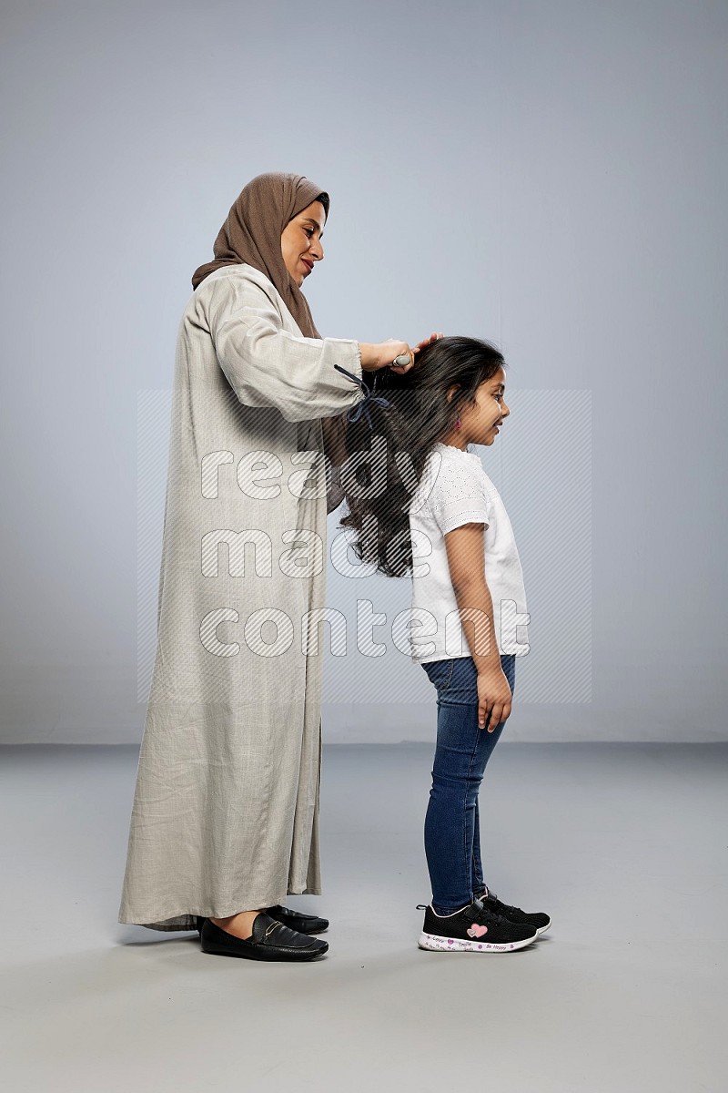 Mom standing styling hair for her daughter on gray background