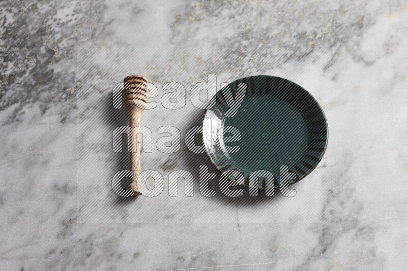 Multicolored pottery plate with wooden honey dipper on the side on grey marble background