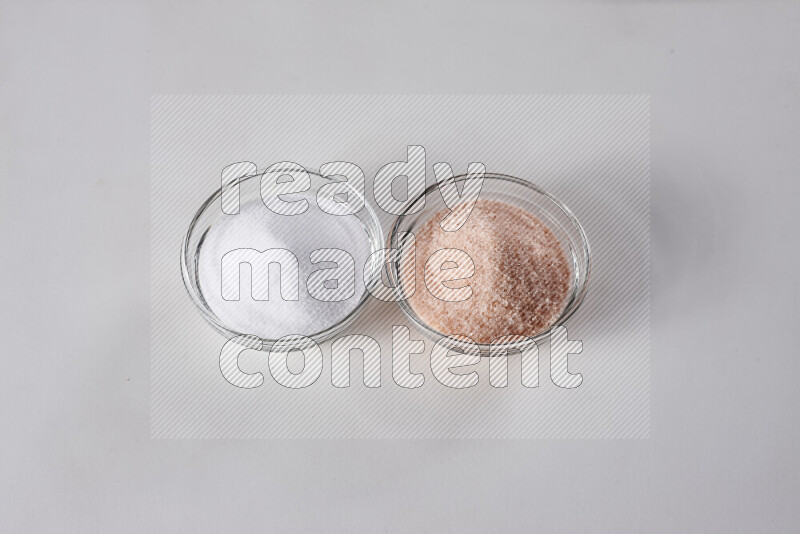 2 glass bowls one is filled with himalayan salt and the other with white salt on white background