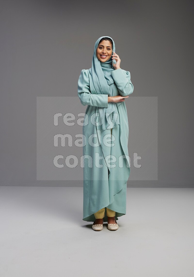 Saudi Woman wearing Abaya standing talking on phone on Gray background