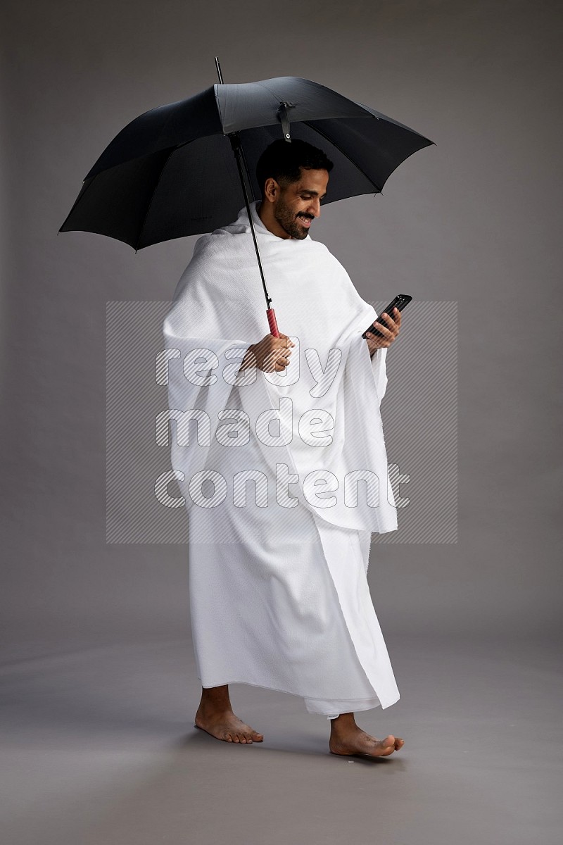 A man wearing Ehram Standing holding umbrella on gray background