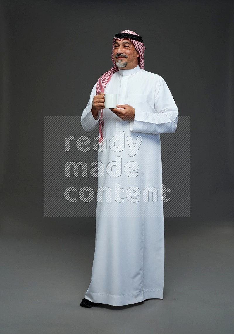 Saudi man with shomag Standing holding mug on gray background