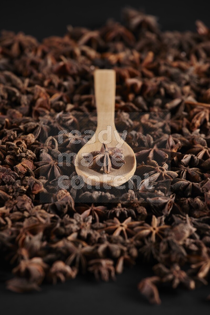 اليانسون النجمي في ملعقة خشبية فوق اليانسون النجمي الذي يغطي الإطار على أرضية سوداء