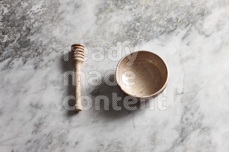 Beige Pottery bowl with wooden honey handle on the side with grey marble flooring, 65 degree angle