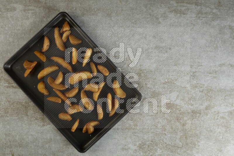 wedges potato in a black stainless steel rectangle tray on grey textured counter top