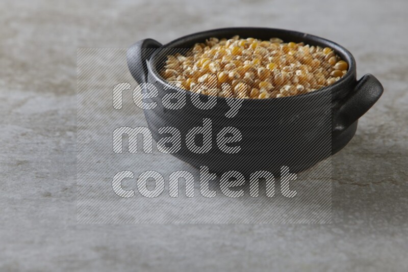 corn kernel in a black handheld ceramic bowl on a grey textured countertop