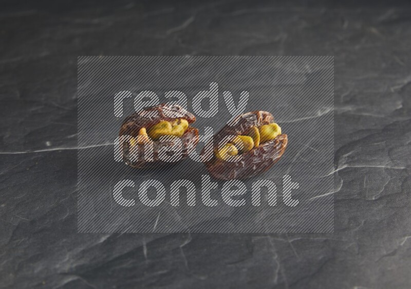 two pistachios stuffed madjoul dates on a black textured background