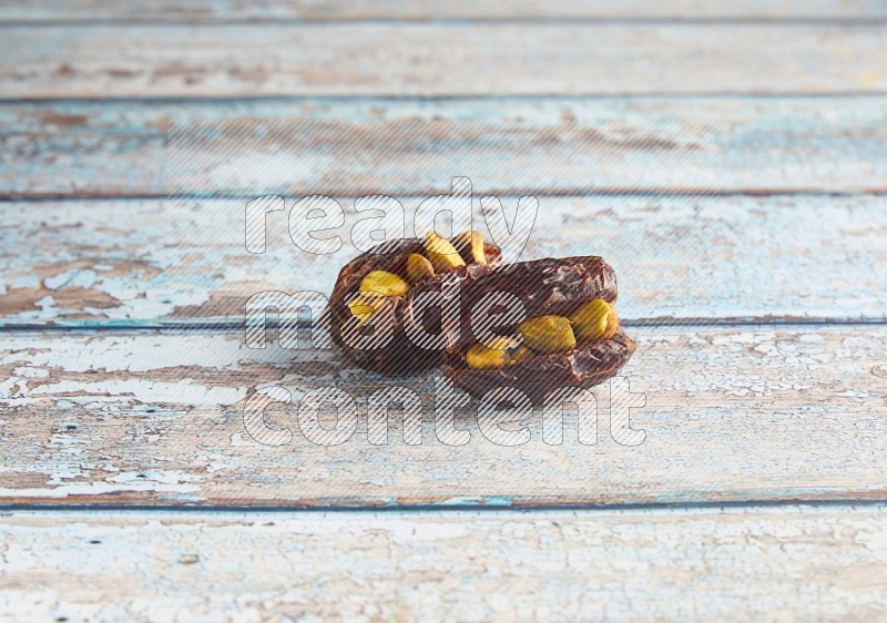 two pistachio stuffed madjoul dates on a light blue wooden background