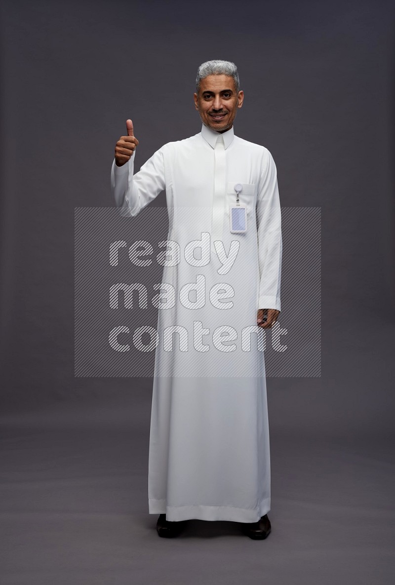 Saudi man wearing thob with pocket employee badge standing interacting with the camera on gray background