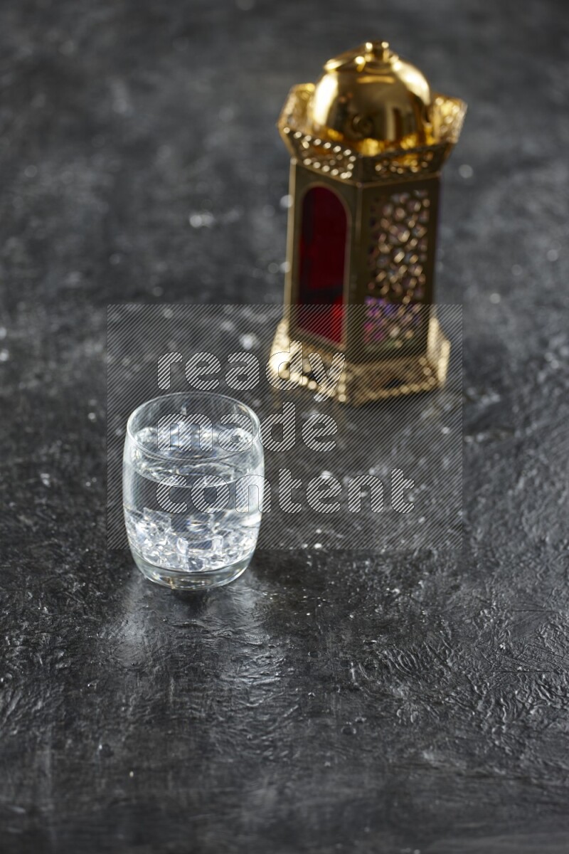 A golden lantern with different drinks, dates, nuts, prayer beads and quran on textured black background