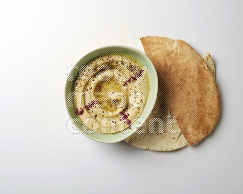 Hummus in a green plate garnished with zattar & sumak on a white background