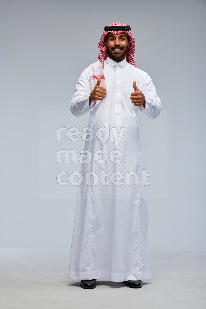 Saudi man Wearing Thob and shomag standing interacting with the camera on Gray background