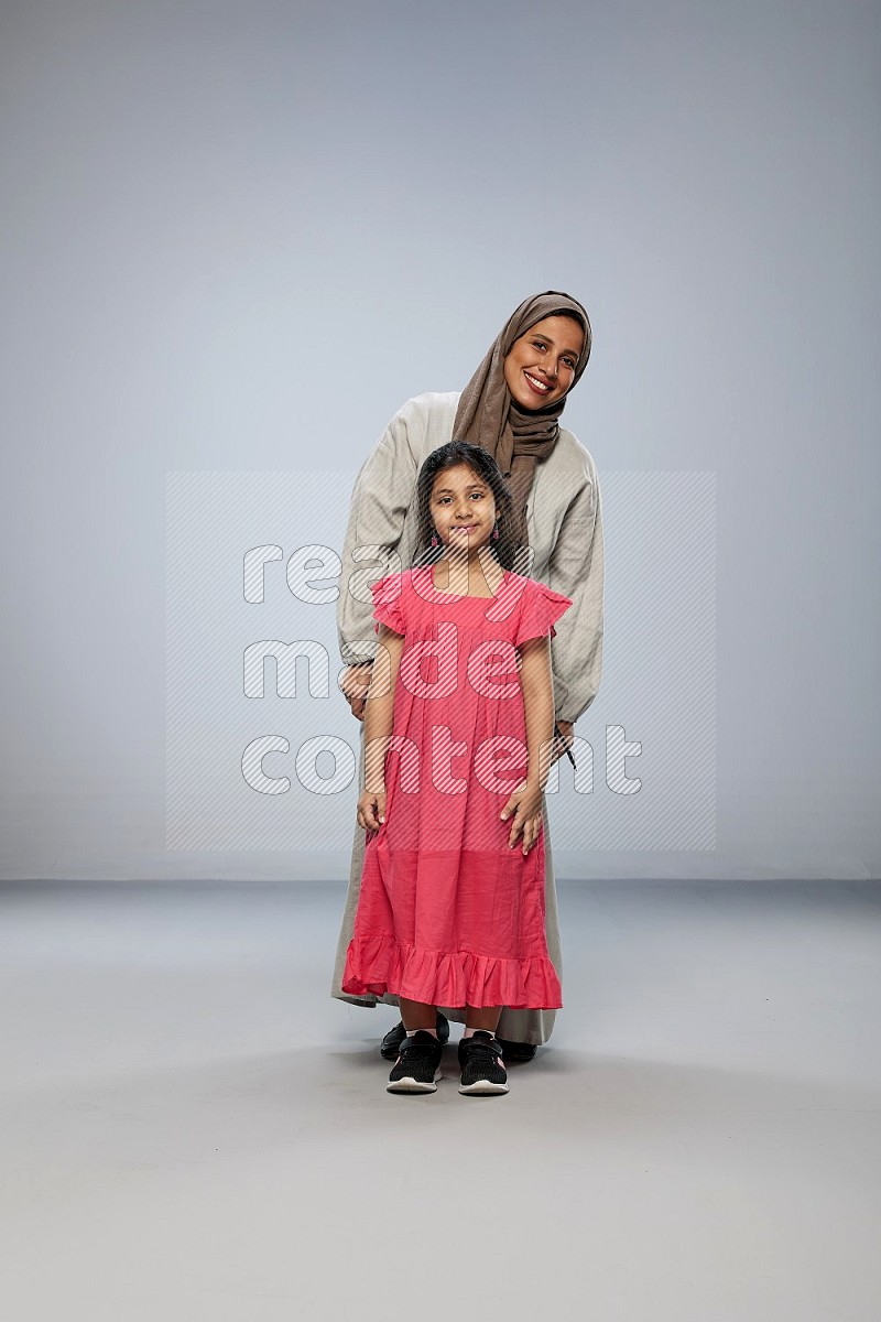 A girl and her mother interacting with the camera on gray background