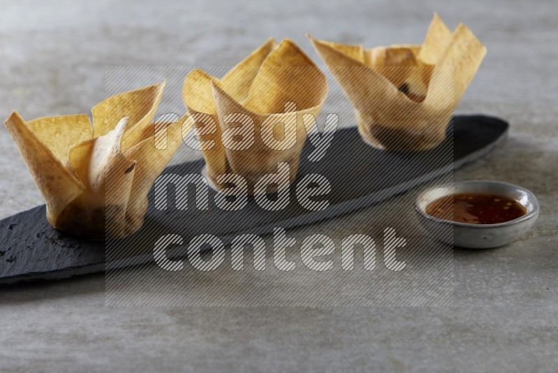 wonton cups with soy sauce ramkin on oval slate on grey textured counter top