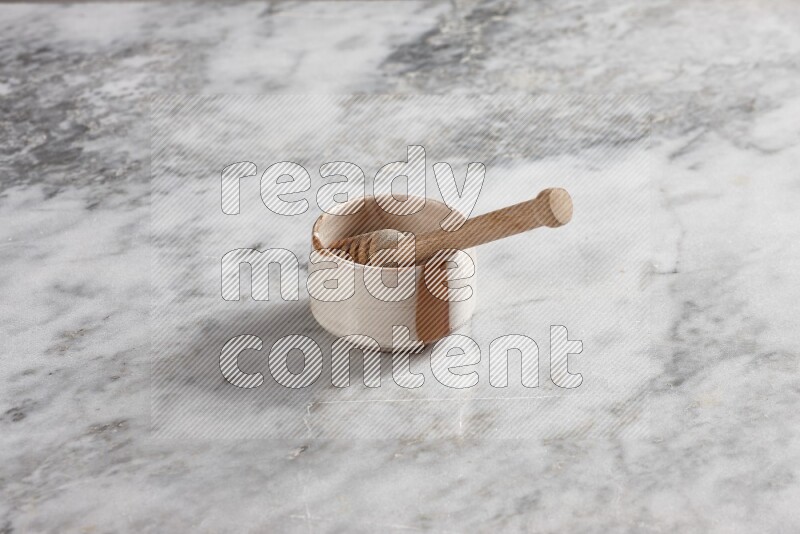 Multicolored pottery bowl with wooden honey dipper in it on grey marble background