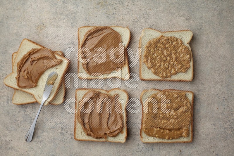 Creamy and Crunchy peanut butter on a white toast with a spreading knife on a light blue textured background