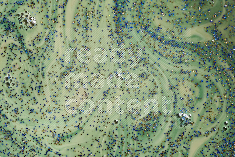 A close-up of sparkling blue and gold glitter scattered on swirling green background