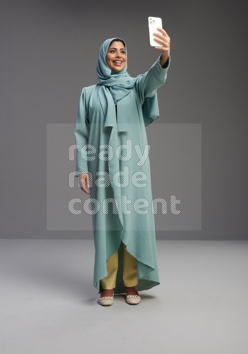 Saudi Woman wearing Abaya standing taking selfie on Gray background