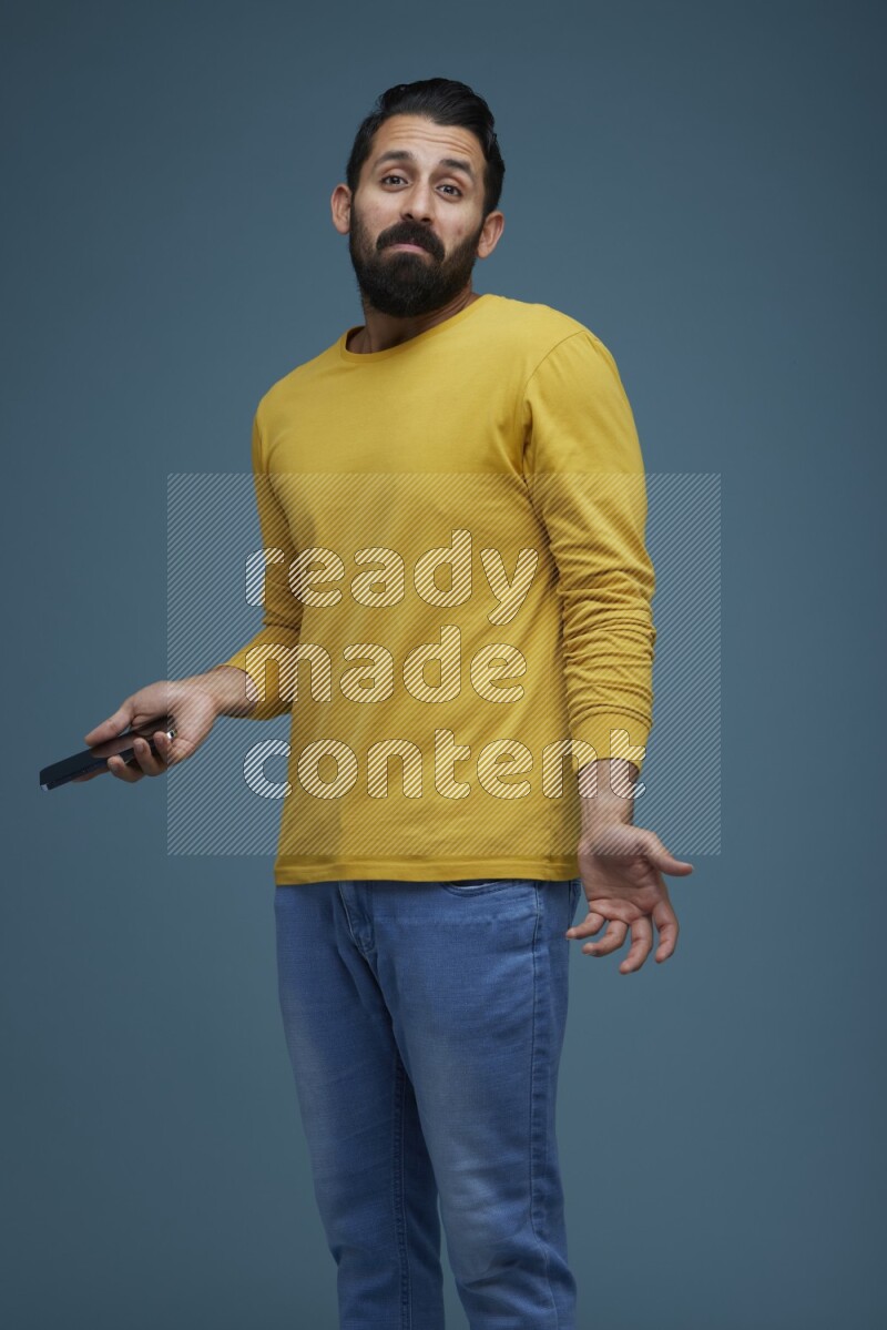 Man posing with a phone in a blue background wearing a yellow shirt