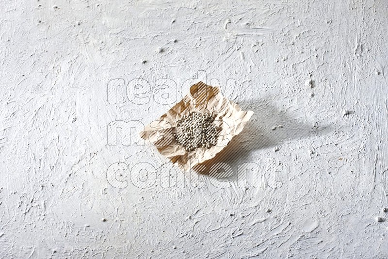 White pepper beads in a crumpled piece of paper on textured white flooring