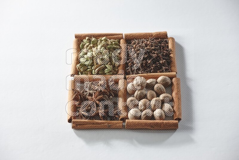 4 مربعات من أعواد القرفة ممتلئة بالهيل واليانسون والقرنفل وجوزة الطيب على أرضية بيضاء