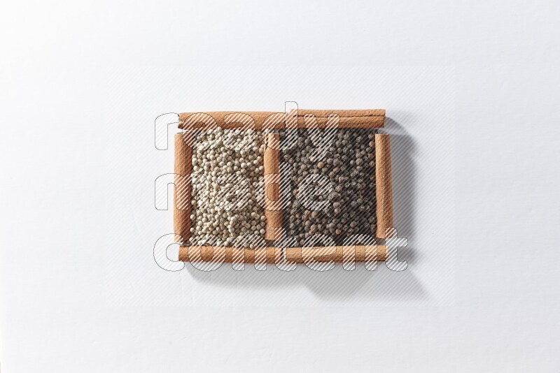 مربعان من أعواد القرفة ممتلئان بحبوب الفلفل الأسود والفلفل الأبيض علي خلفية بيضاء