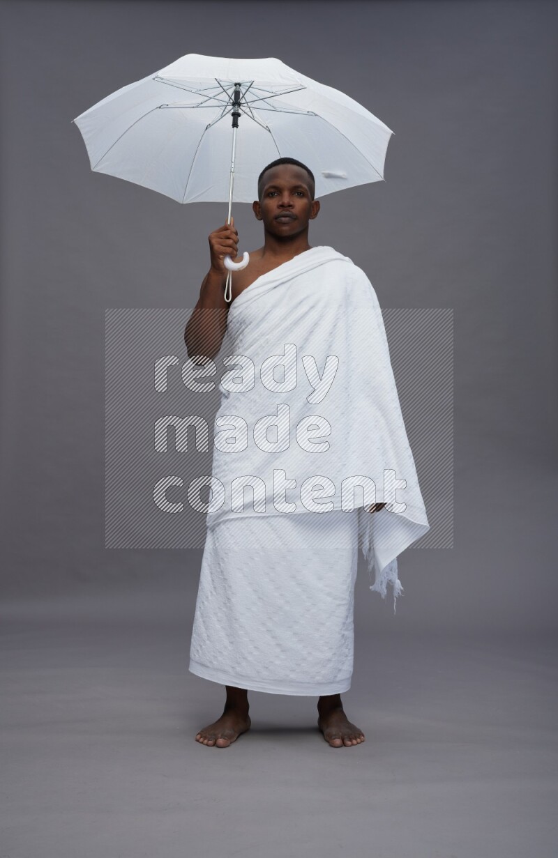 A man wearing Ehram Standing holding umbrella on gray background