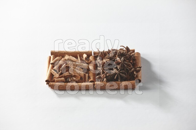 مربعان من أعواد القرفة ممتلئان باليانسون النجمي وقطع من القرفة علي خلفية بيضاء