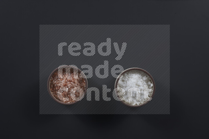 2 وعاء فخاري احدهمها ممتلئ بملح الهيمالايا والأخر بالملح الأبيض على خلفية سوداء