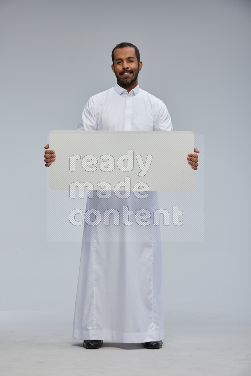 Saudi man wearing Thob standing holding board on Gray background
