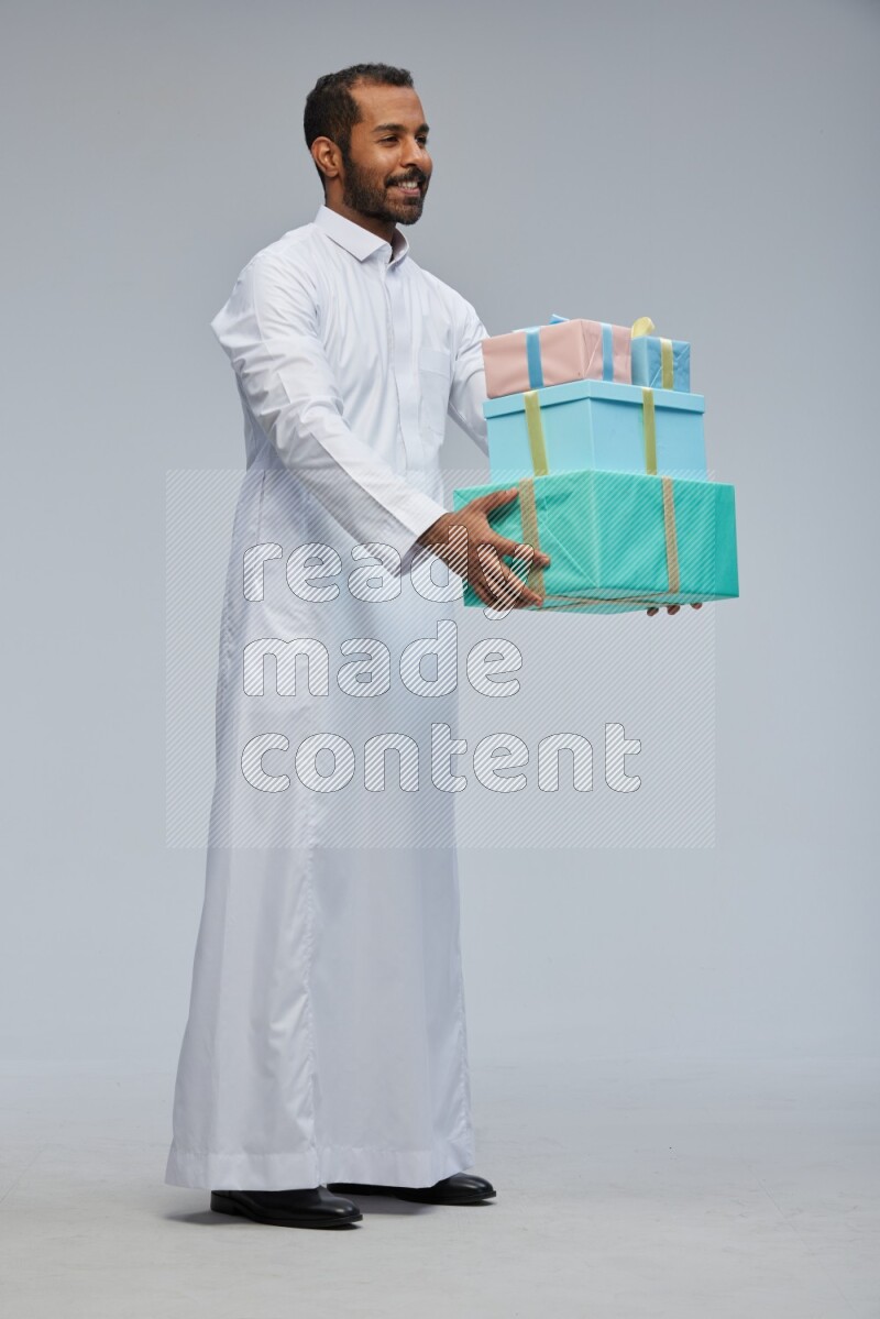 Saudi man Wearing thob standing holding gift box on Gray background
