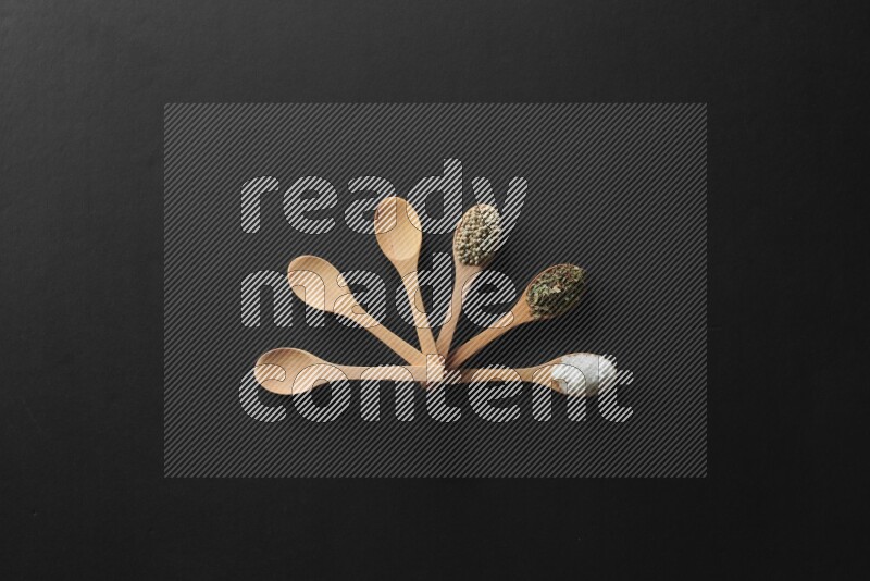 الفلفل الأبيض والقرنفل والهيل والملح والفلفل الأسود وريحان مجفف في معالق خشبية علي خلفية سوداء