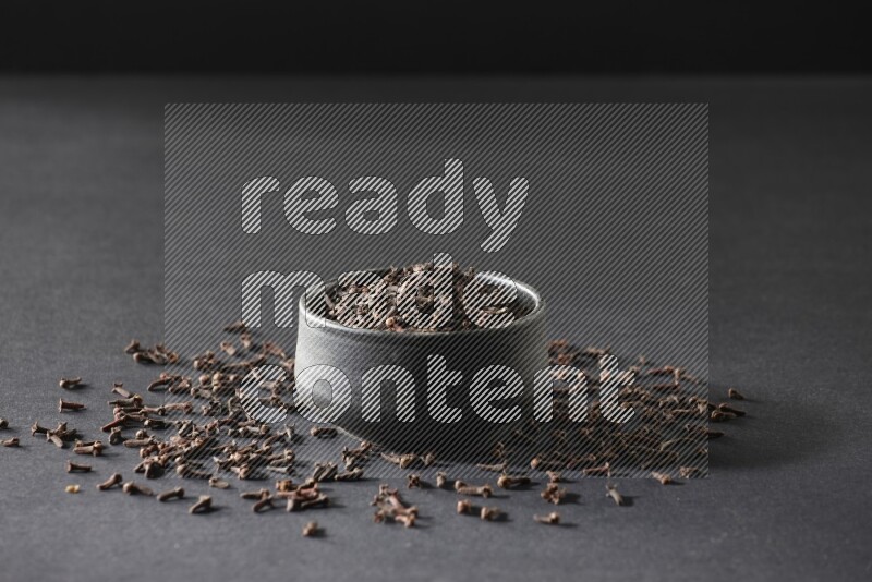 A black pottery bowl full of cloves on a black flooring