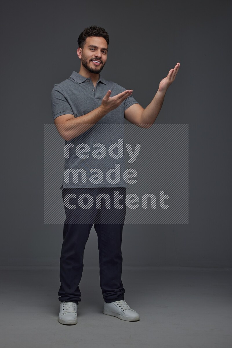 A man wearing casual standing and making multi hand gestures eye level on a gray background