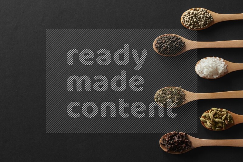 الفلفل الأبيض والقرنفل والهيل والملح والفلفل الأسود وريحان مجفف في معالق خشبية علي خلفية سوداء