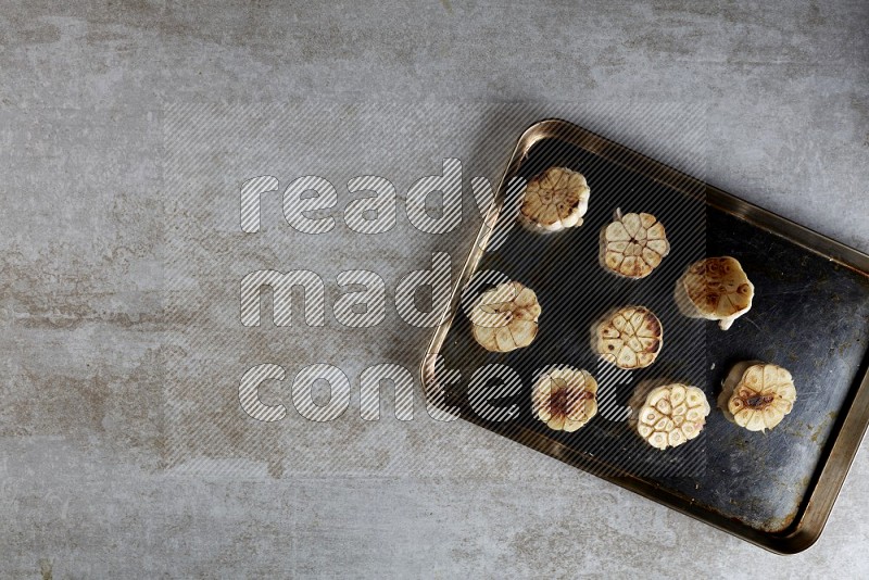 half's roasted garlic in a stainless tray on a grey textured countertop