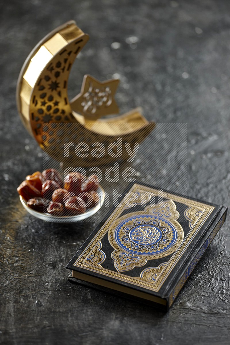 A wooden golden crescent lantern with different drinks, dates, nuts, prayer beads and quran on textured black background