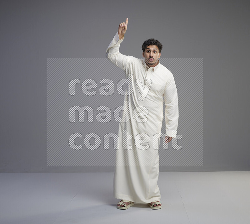 A Saudi man standing wearing thob interacting with the camera on gray background