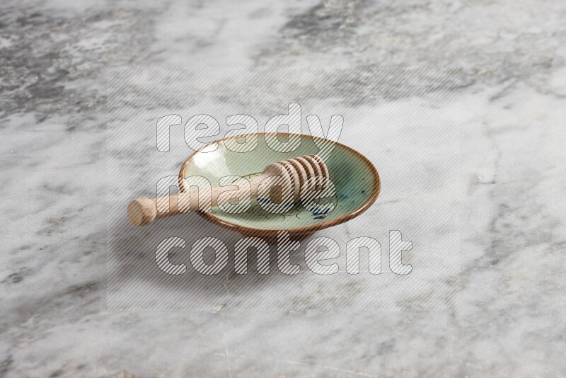 Decorative pottery plate with wooden honey dipper in it on grey marble background
