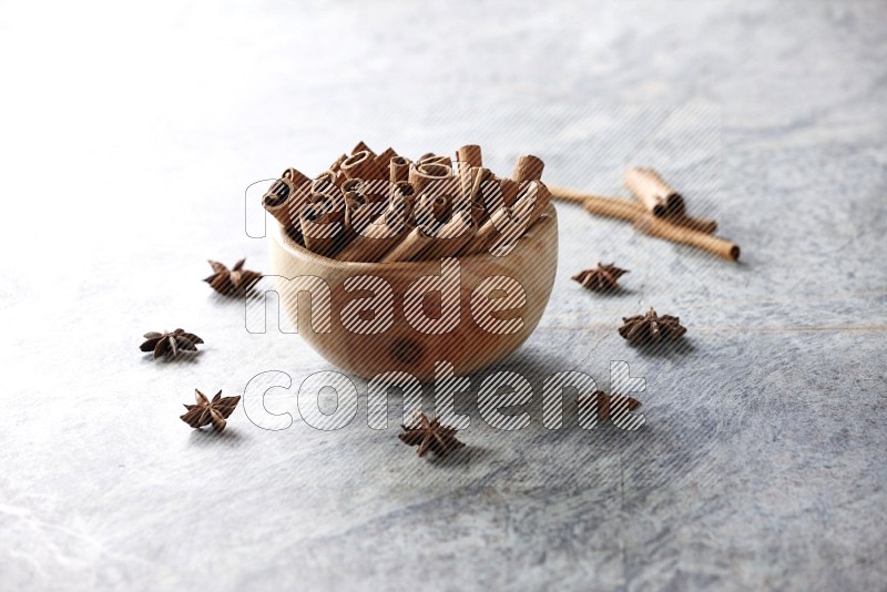 wooden bowl full of cinnamon sticks surrounded by star anis on marble background in different angles