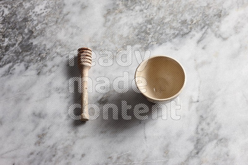 Beige Pottery bowl with wooden honey handle on the side with grey marble flooring, 65 degree angle