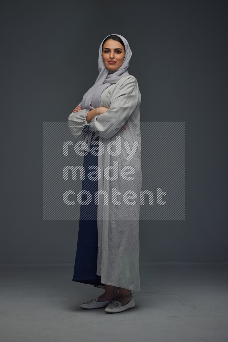 A Saudi woman wearing a light gray Abaya and head scarf standing and making multi poses eye level on a grey background