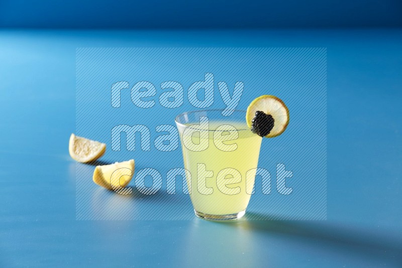 glass of lemon juice with lemon slice and berry on blue background